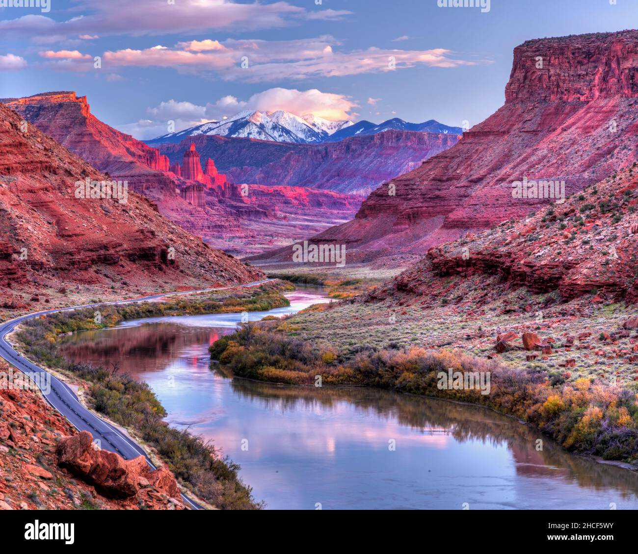 The Colorado River winds its way toward Fisher Towers glowing pink in the late afternoon Autumn light with the snow-capped La Sal Mountains behind. Stock Photo