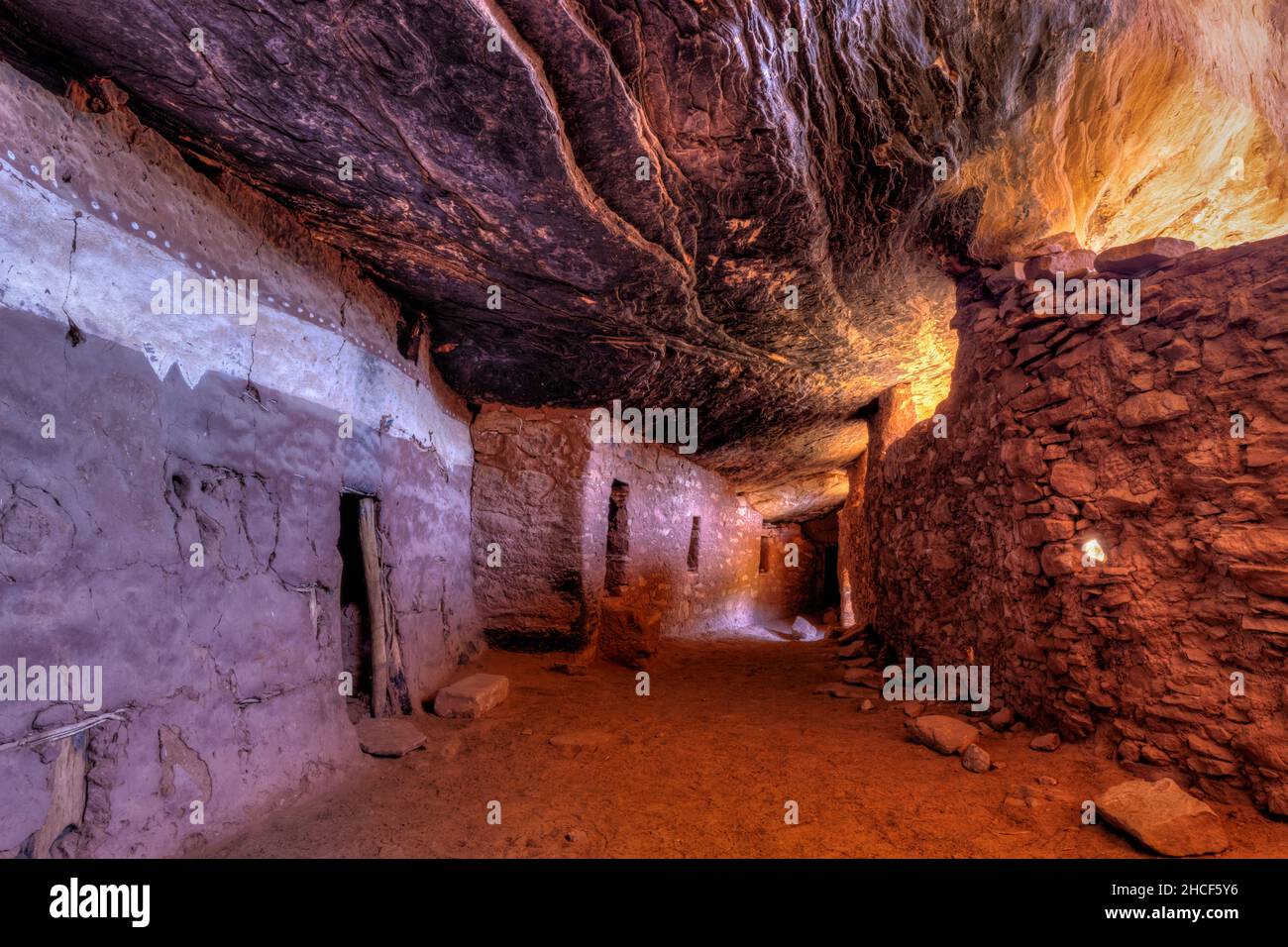 Indirect bounce light creates interesting colors in an ancient interior hallway below a sloping layered cliff wall in the late 13th century Moon House Stock Photo
