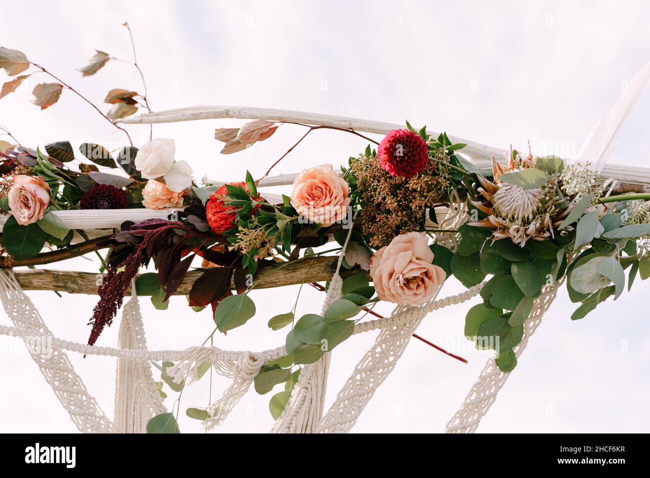 Top of the wedding arch decorated with macrame, roses, celosias and green leaves Stock Photo