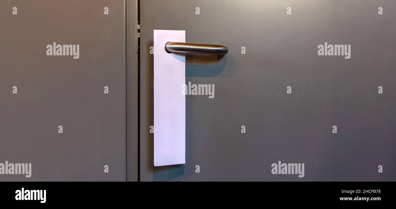 Door knob with blank hanger mock up. Empty white tag for text or room number hang on a closed door handle, copy space. Hotel Dont disturb sign. Stock Photo