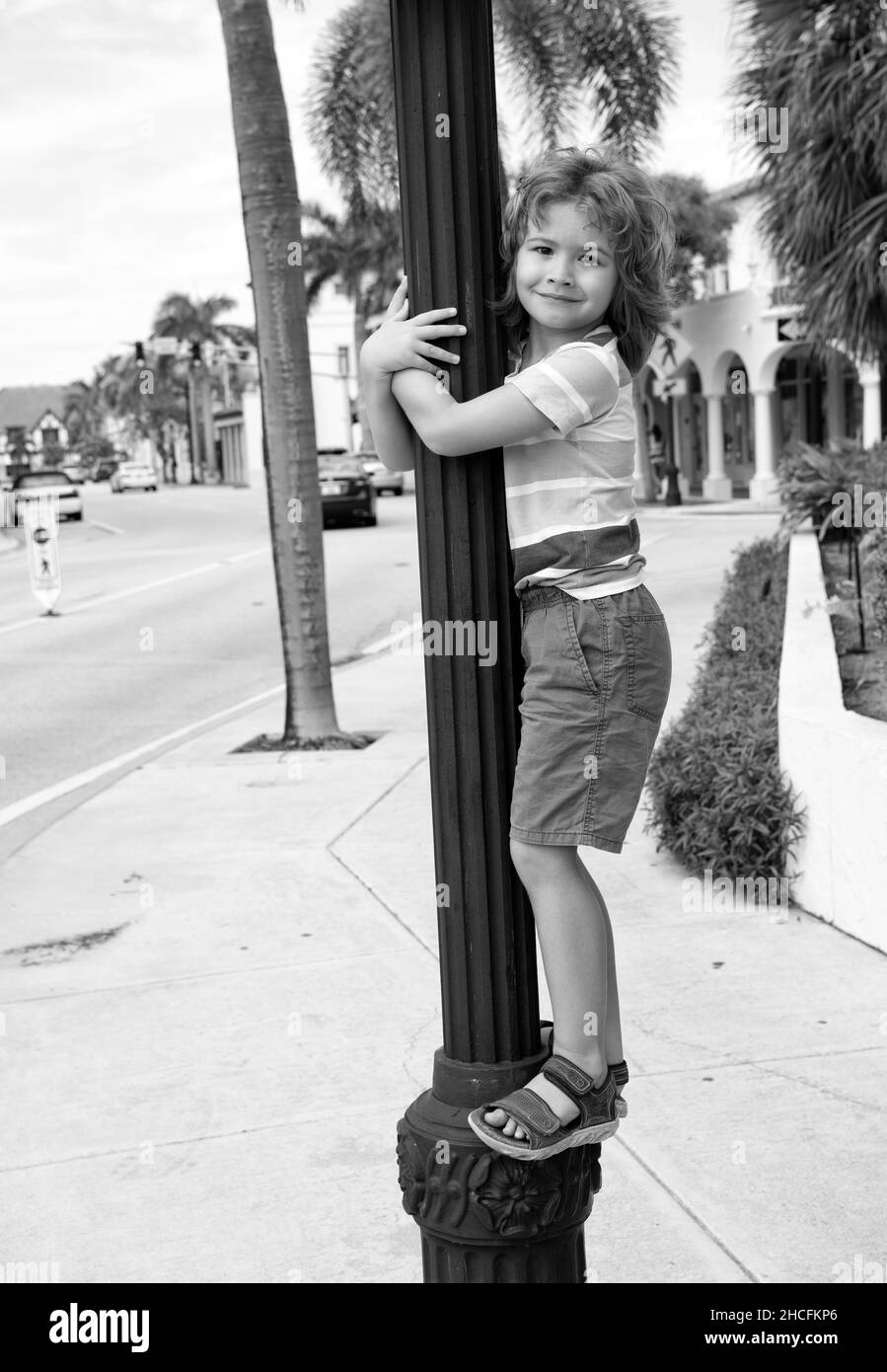 Energetic boy child climb up street lamppost summer outdoors, childhood Stock Photo