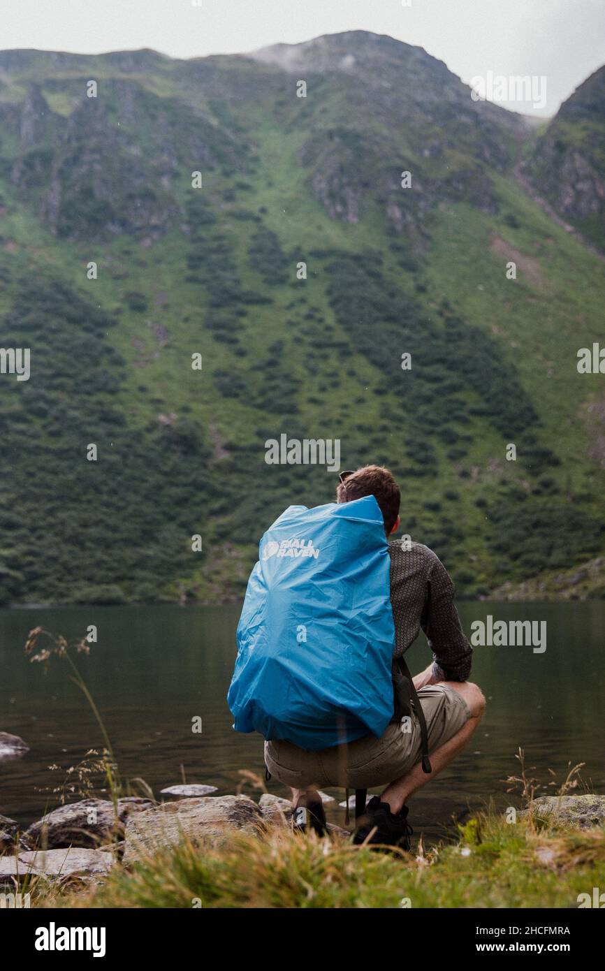 Vertical shot of a man watching over a lake with Fjallraven bag Stock Photo