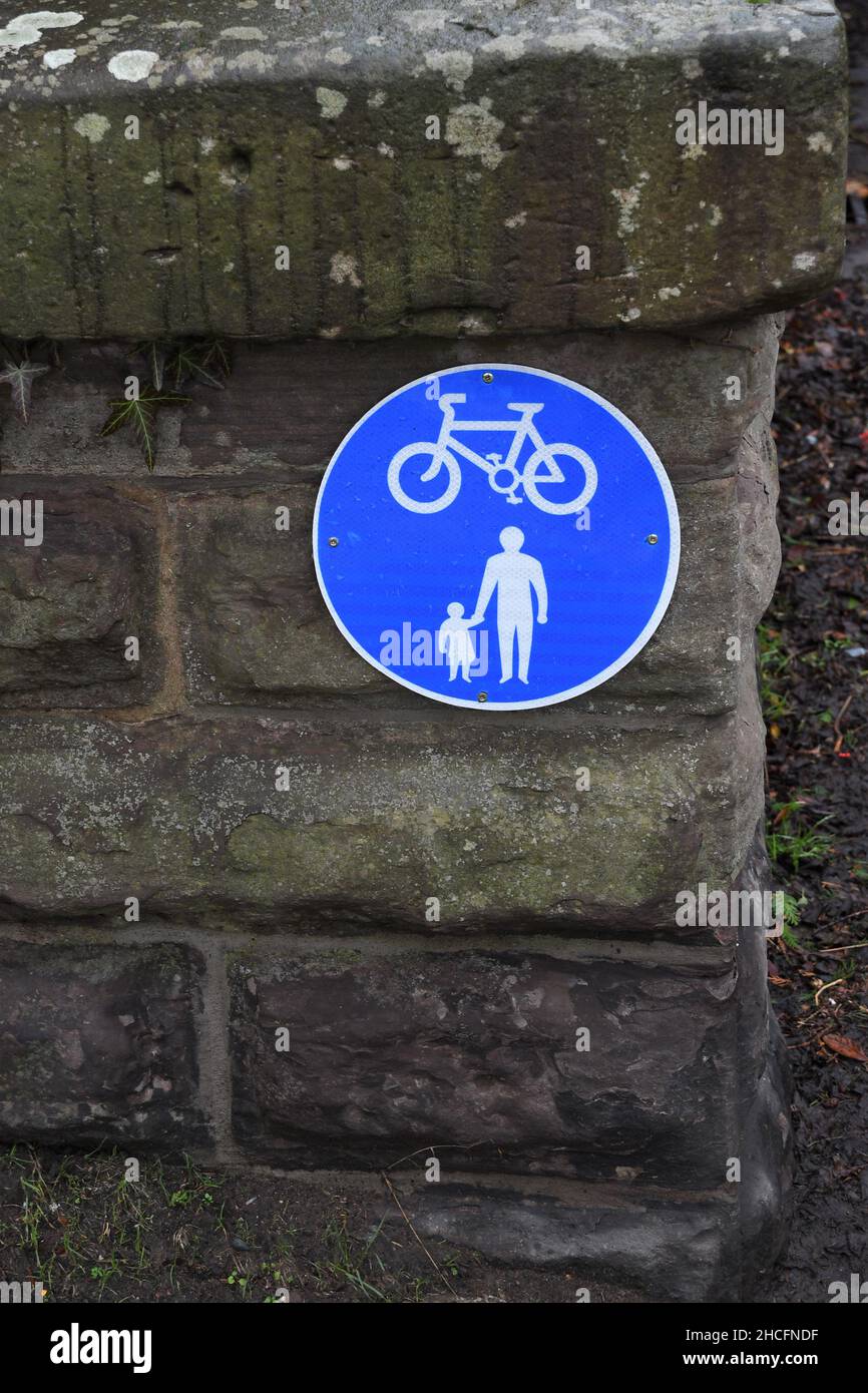 Bicycle and pedestrian lane road sign on stone wall. Large blue round circular sign with isolated bike and parent with child. Stock Photo