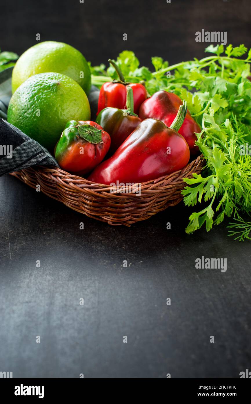 Some fresh red chili pepper and lemons in a basket with fresh coriander on a black wooden table Stock Photo
