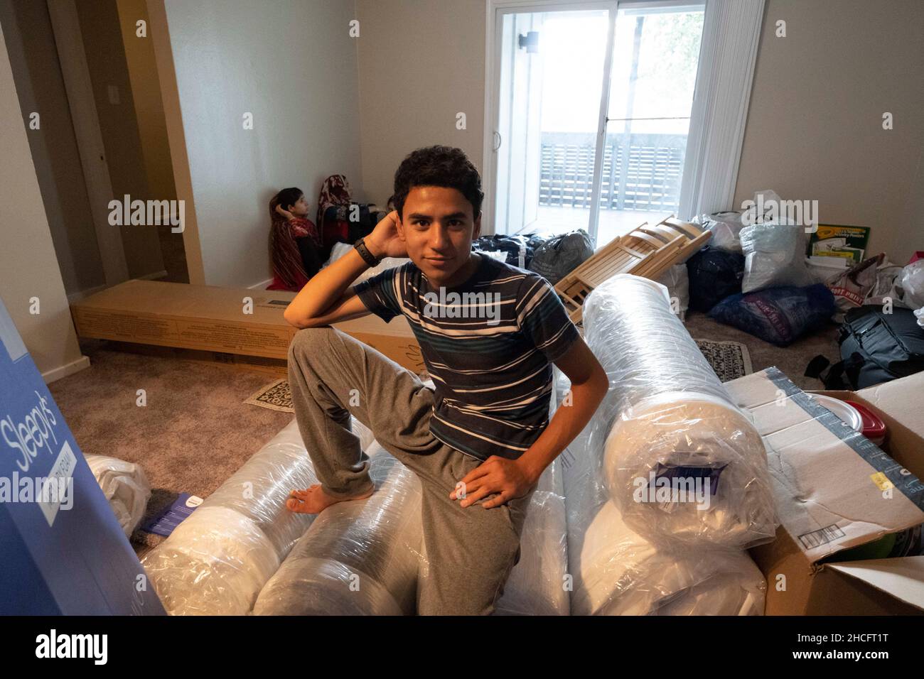 Austin Texas USA, October 2021: Afghan teen poses with rolled-up new mattresses in his family's new apartment in a complex near downtown. Refugees fleeing turmoil in Afghanistan continue to be resettled in Texas with many single men and large families with children moving into apartments across Austin. Faith-based and other non-profit groups have stepped up to help coordinate efforts in furnishing homes for hundreds of refugees. ©Bob Daemmrich Stock Photo