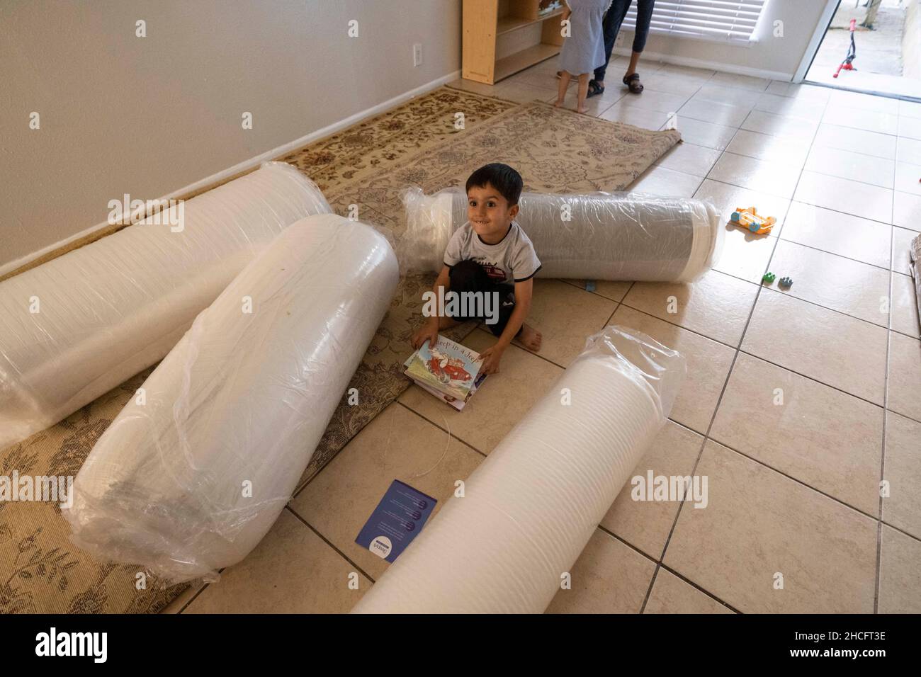 Austin Texas USA, October 2021: Afghan childposes with rolled-up new mattresses in his family's new apartment in a complex near downtown. Refugees fleeing turmoil in Afghanistan continue to be resettled in Texas with many single men and large families with children moving into apartments across Austin. Faith-based and other non-profit groups have stepped up to help coordinate efforts in furnishing homes for hundreds of refugees. ©Bob Daemmrich Stock Photo