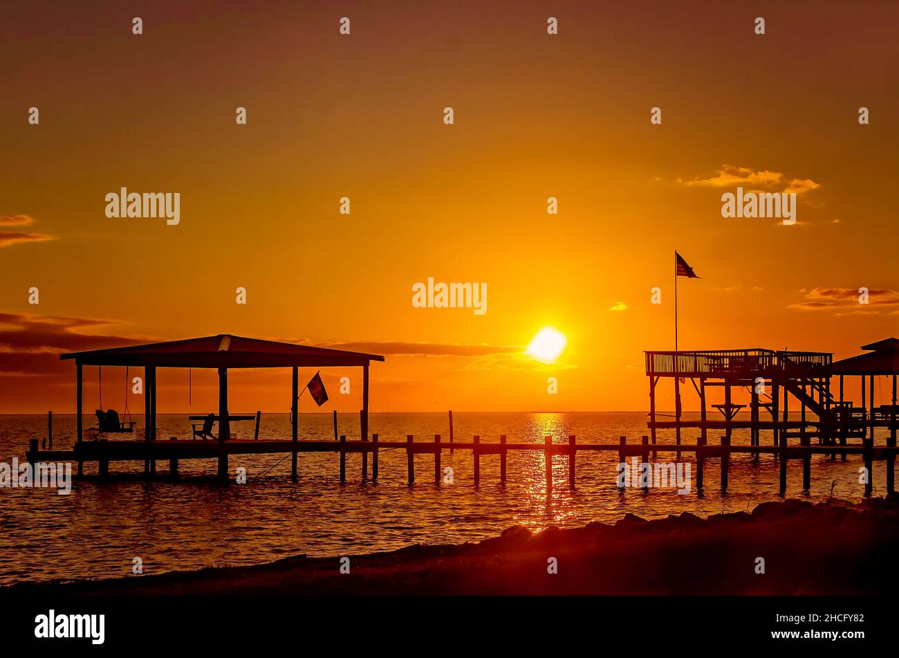 The sun sets behind boat docks and fishing piers on Coden Beach, Dec