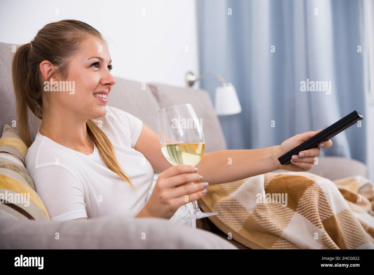Young female is watching TV and sitting with white wine Stock Photo - Alamy