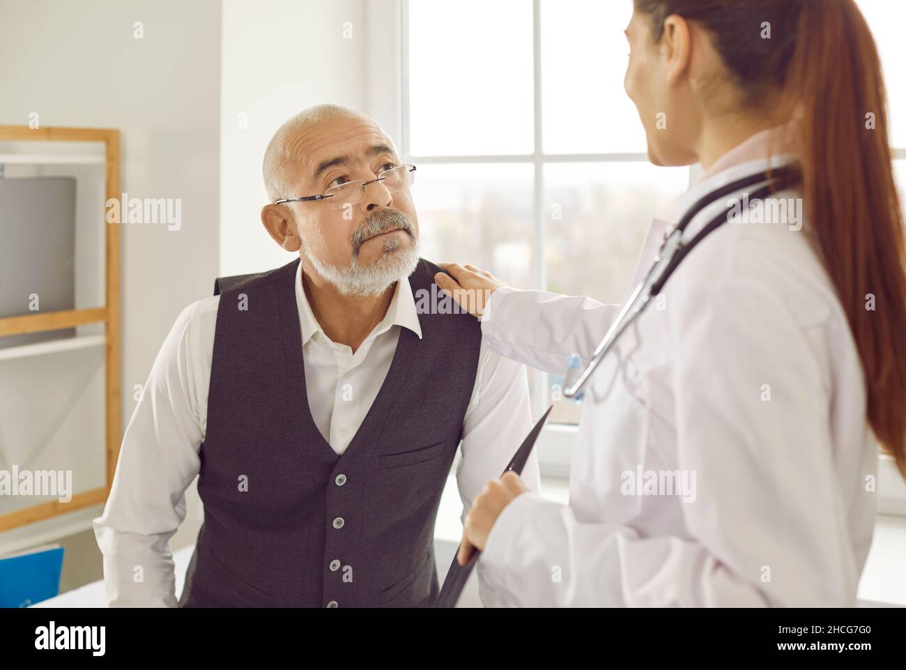 Doctor puts her hand on her senior patient's shoulder to reassure and support him Stock Photo