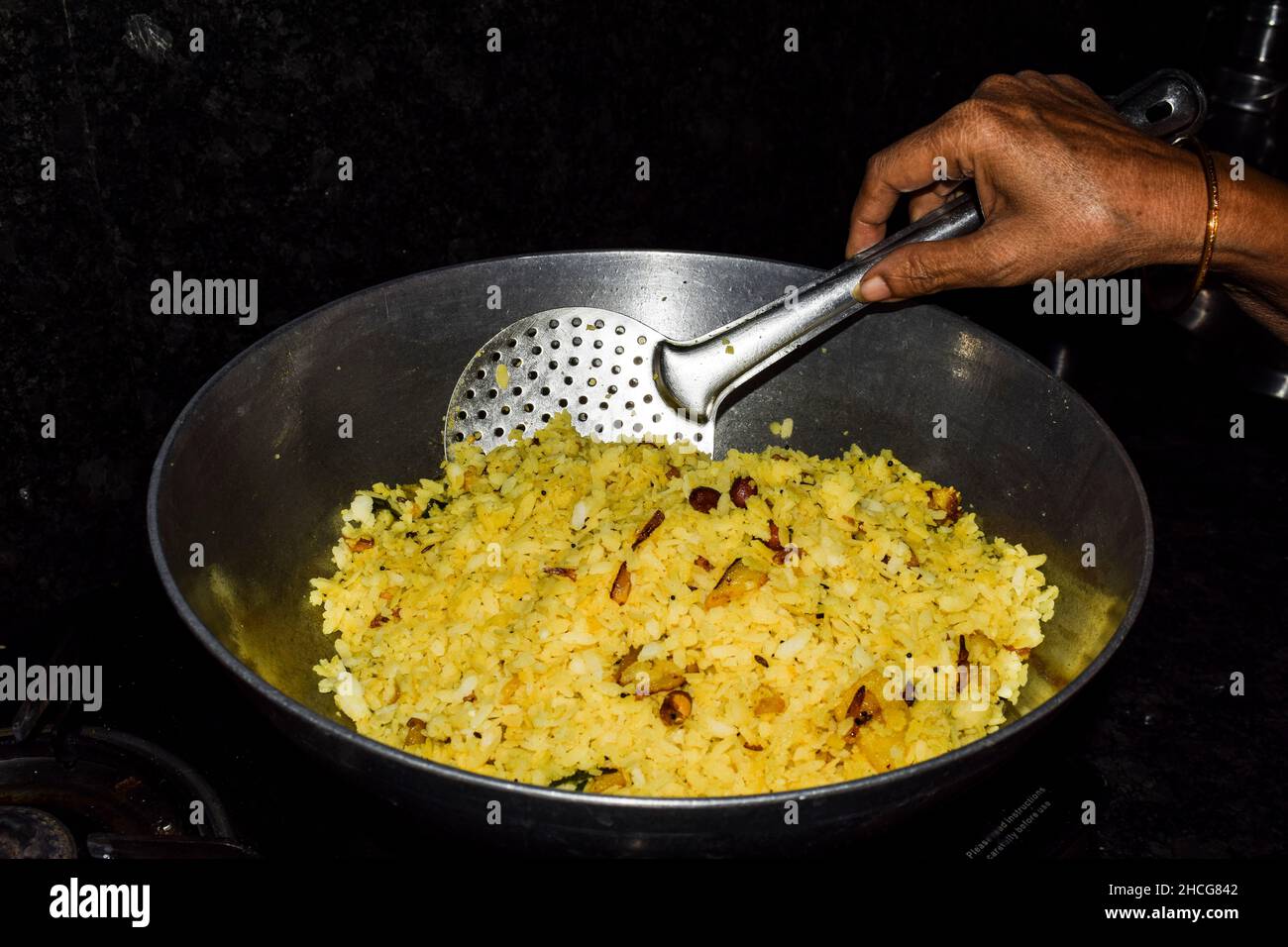 Woman cooking delicious Kanda poha, maharastrian dish in home kitchen. Soaked white beaten rice and frying onions, green chillies, curry leaves, turme Stock Photo