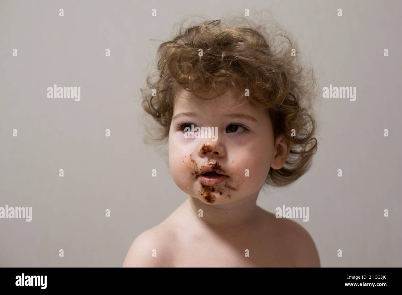 Portrait of a little girl 1 year old, face smeared with chocolate. The child pulled off a chocolate bar and smeared his lips and cheeks. Girl with cur Stock Photo