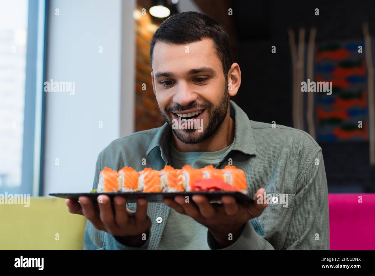 amazed man holding plate with set of tasty sushi rolls in restaurant Stock Photo