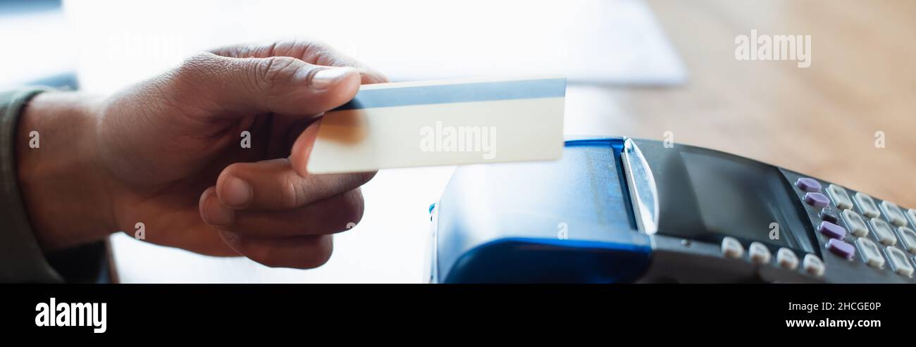 cropped view of man holding credit card near payment terminal in cafe, banner Stock Photo