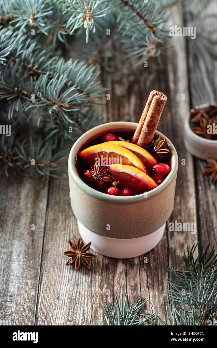 Mulled vine with spices, orange slices and cranberry in ceramic glass on wooden background with gravy boat with cranberries Stock Photo