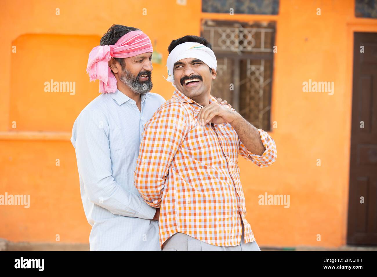 Two happy cheerful indian farmer having fun with each other with outside their village house, Men friends wearing traditional kurta and head wrap clot Stock Photo