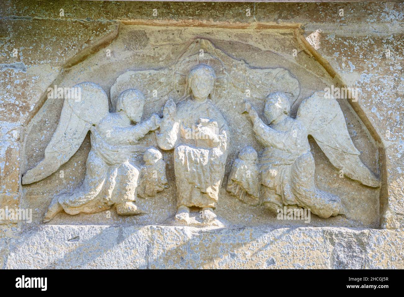 12th century Norman tympanum showing Christ and 2 ministering angels in the wall of St Peters church in the Cotswold village of Little Barrington UK Stock Photo