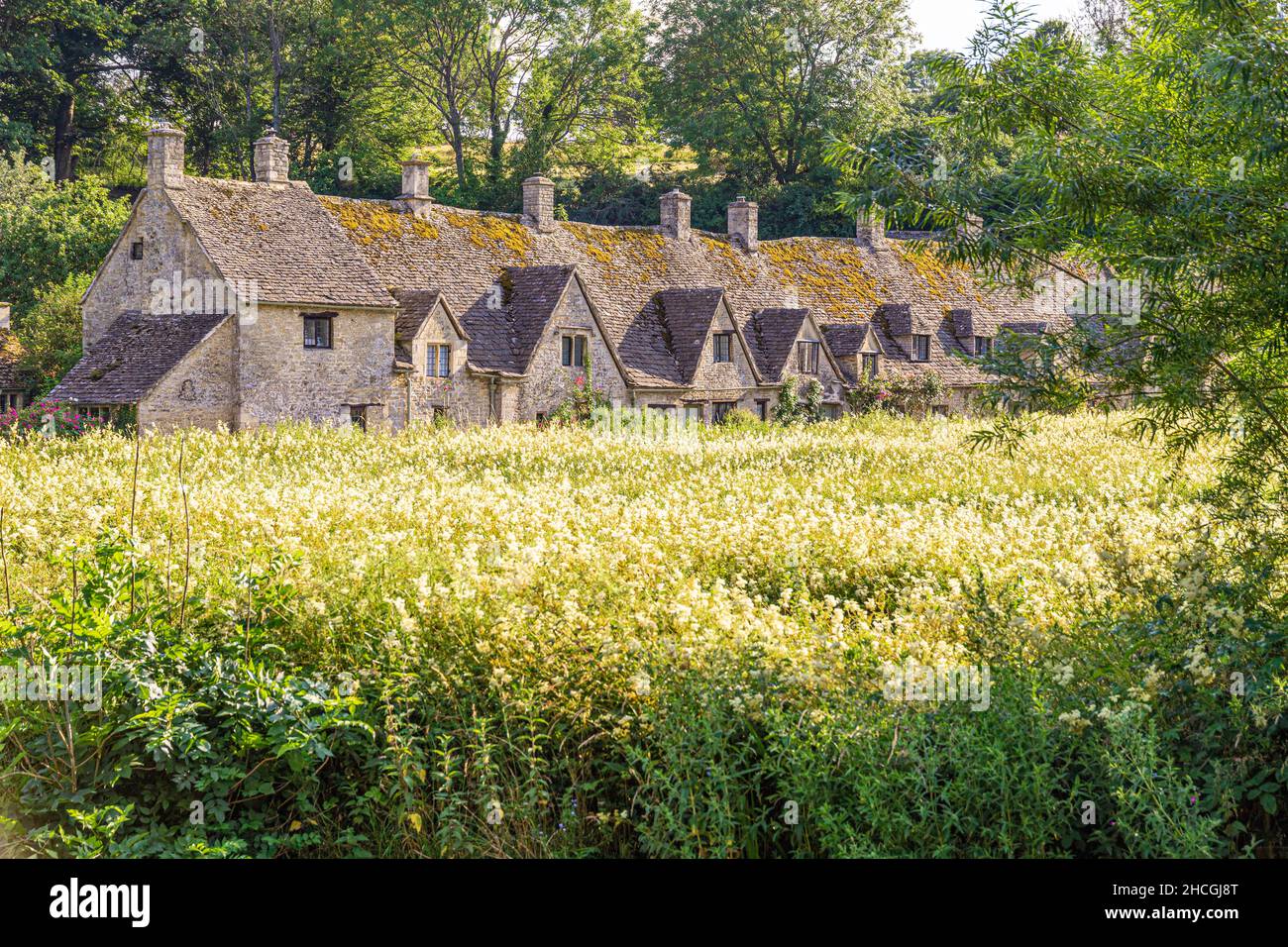 Evening light falling on Arlington Row, 14th century weavers cottages in the Cotswold village of Bibury, Gloucestershire UK. Viewed across Rack Isle. Stock Photo