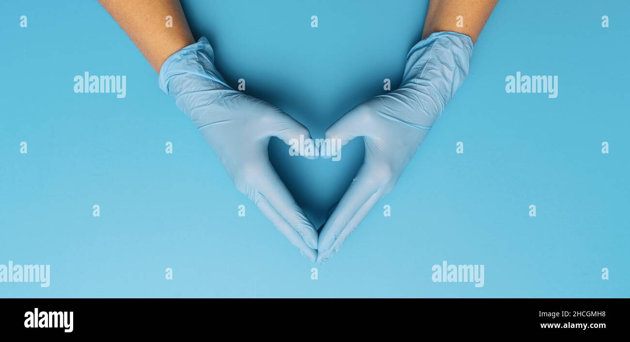 Thanks you doctors in the Corona pandemic, horizontal banner with copy space for text. Female hands in blue gloves show symbol of heart shape on blue Stock Photo