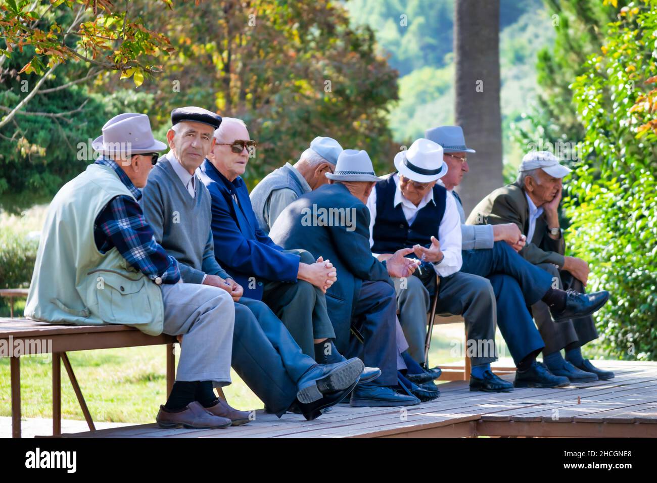 Many older gentlemen with hats are sitting on bench on the park and socialising .Albania Stock Photo