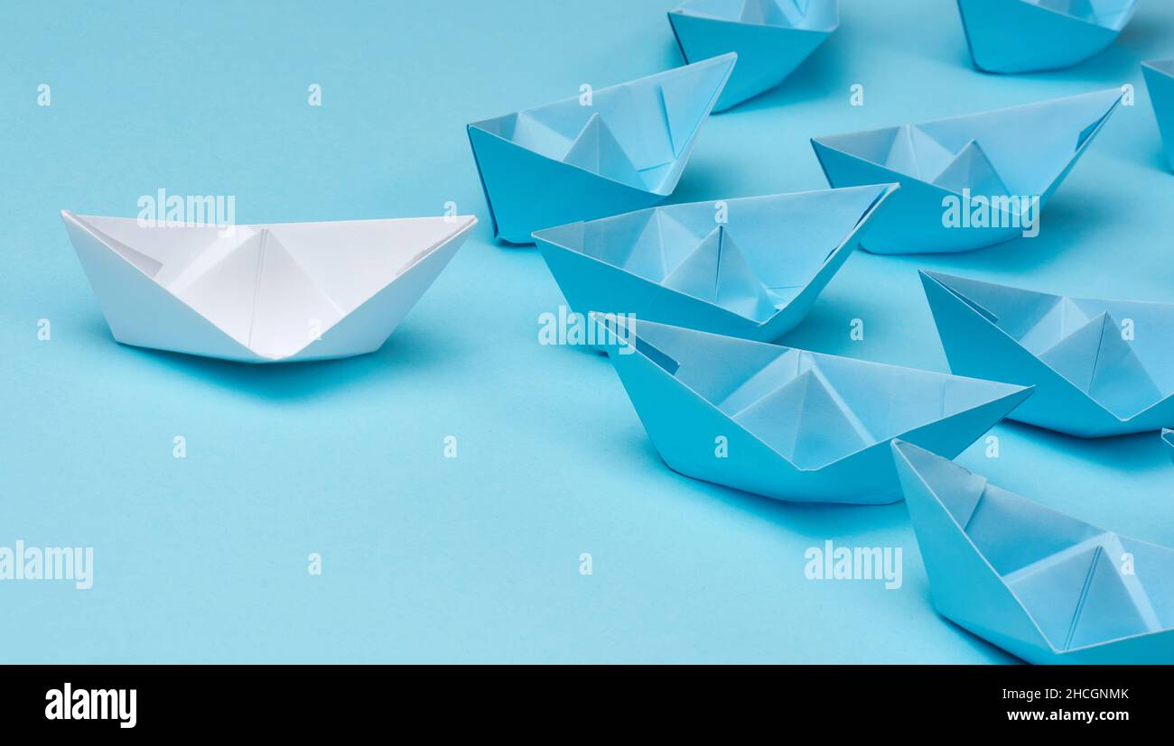 group of blue paper boats follow white against a light blue background. Strong leader concept, mass manipulation. Starting a business with a well-coor Stock Photo