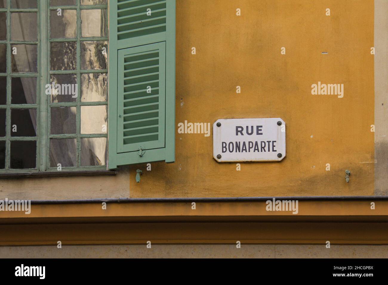 Detail of yellow mediterranean building with green wooden windows and a white street sign saying Rue Bonaparte. Stock Photo