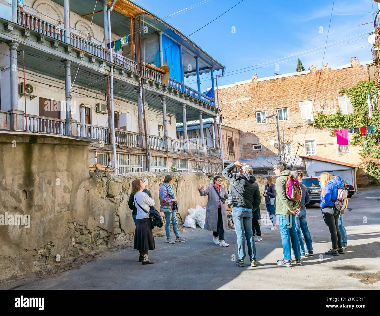 Female tour guide is showing old neighborhood buidings in Tbilisi. Tourism and free walking tours in  Sakartvelo (Georgia). 03.03.2020. Stock Photo