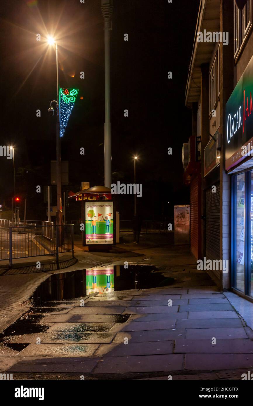 Bus stop with Neon Sign reflecting in a puddle on Wellingborough road