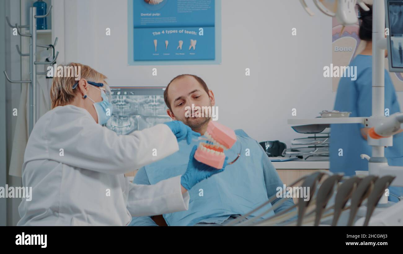 Stomatologist using artificial jaw to explain correct way to brush