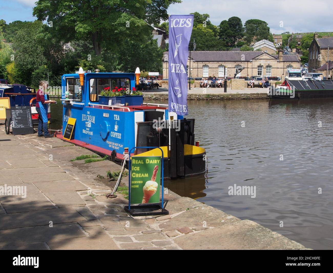 The ice cream boat with a female customer in the sunshine at the canal basin on the Leeds and Liverpool canal in Skipton, North Yorkshire, England. Stock Photo