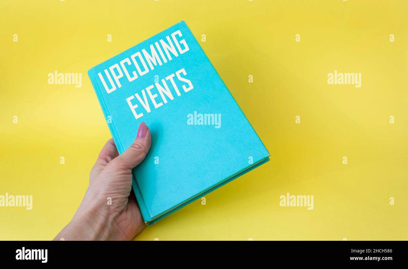 Female hand holding green diary with text sign showing upcoming events on yellow background.Conceptual photo of upcoming planned public or social even Stock Photo