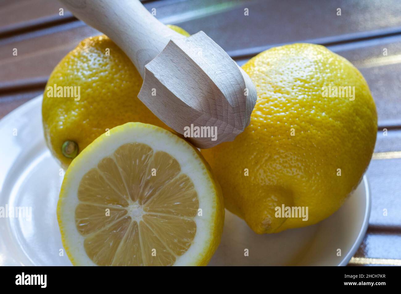 Three yellow lemons on a plate, wooden citrus juicer, halved lemon