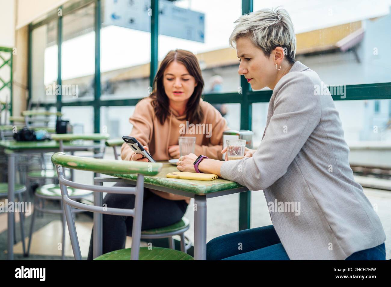 Two women chatting and showing something on the phone in the cafe at train station, Portugal Stock Photo