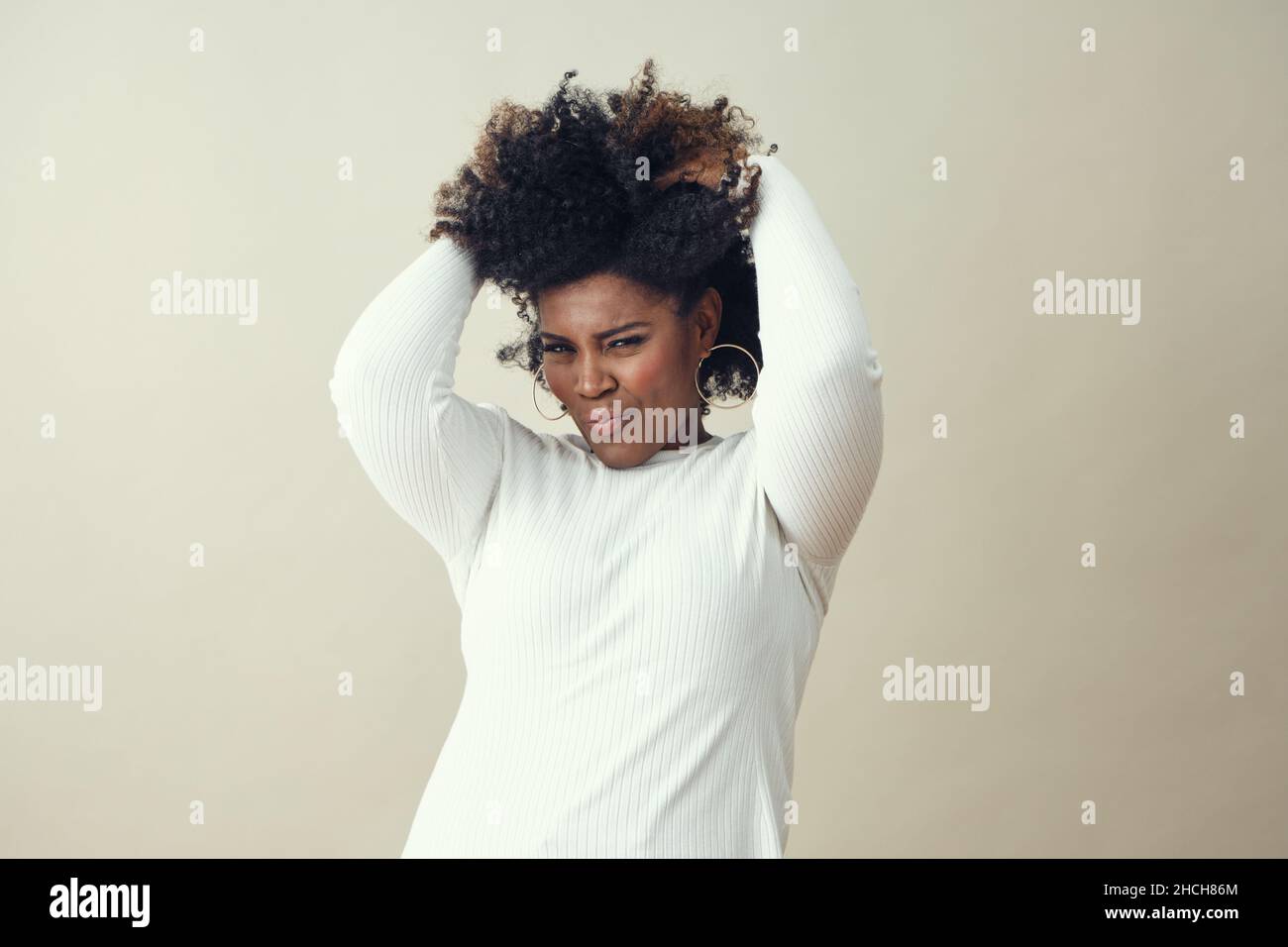 Cheerful Afro woman with hands in hair smiling against white background ...