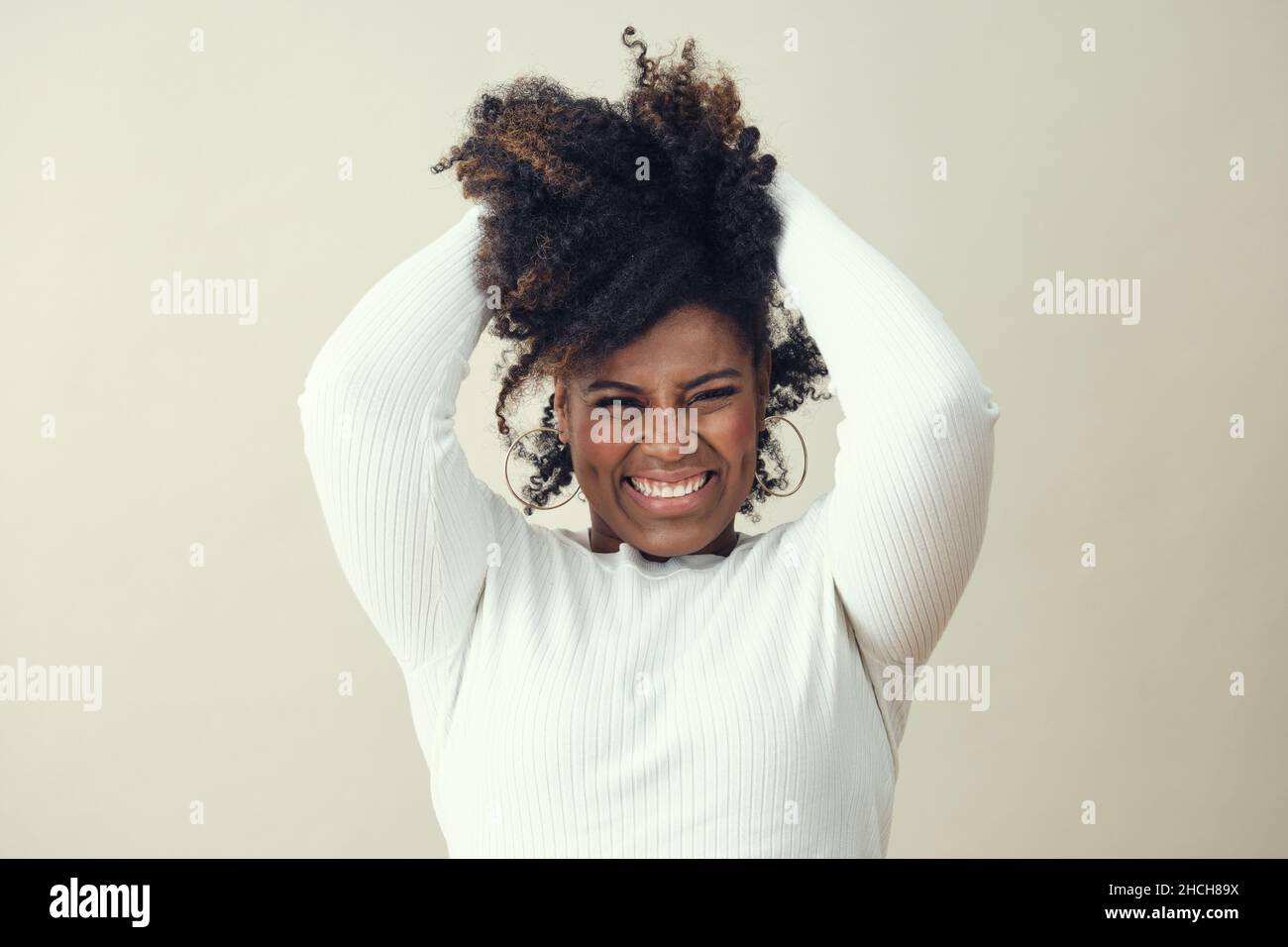 Cheerful Afro woman with hands in hair smiling against white background ...