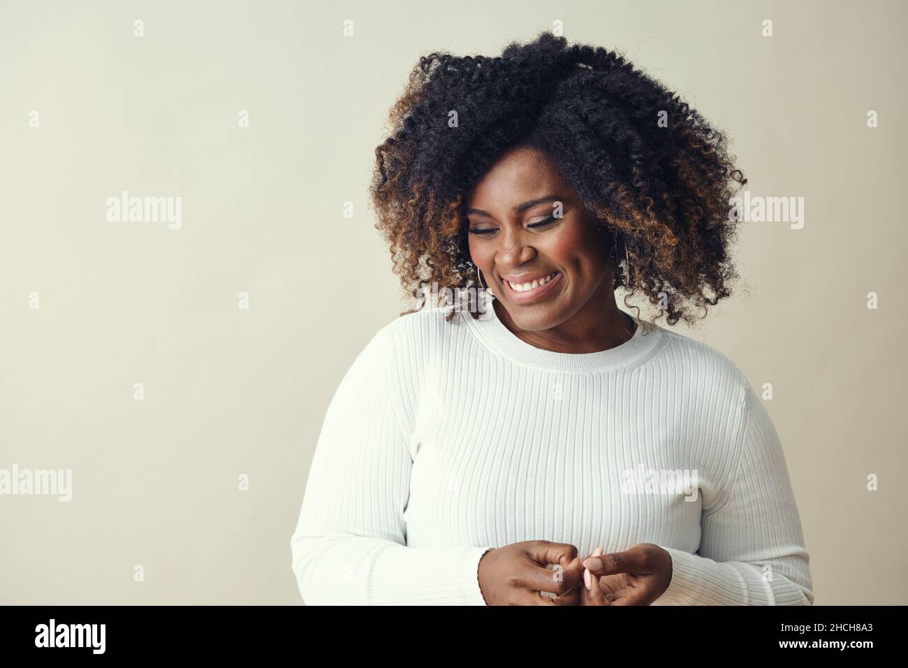 Smiling Afro woman with brown highlights on curly hair looking down against  white background Stock Photo - Alamy