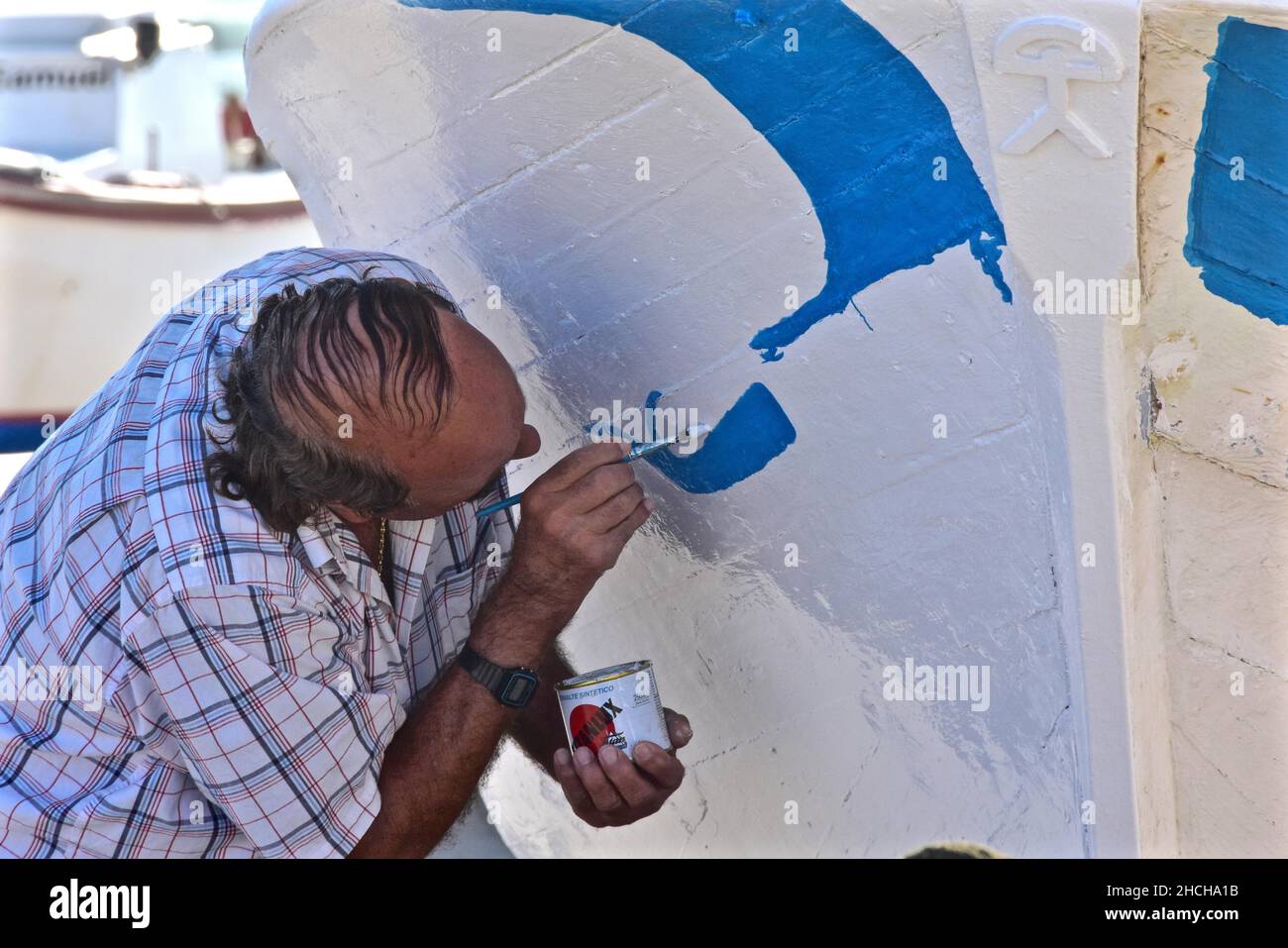 Man with thinning hair paints bow of boat with white and blue paint Stock Photo