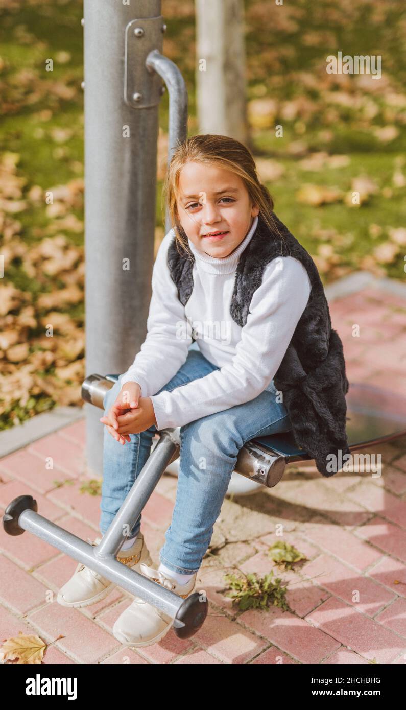 Close-up of a smiling Caucasian girl sitting on a senior exercise equipment in the park on a sunny day. Fitness park concept. Stock Photo