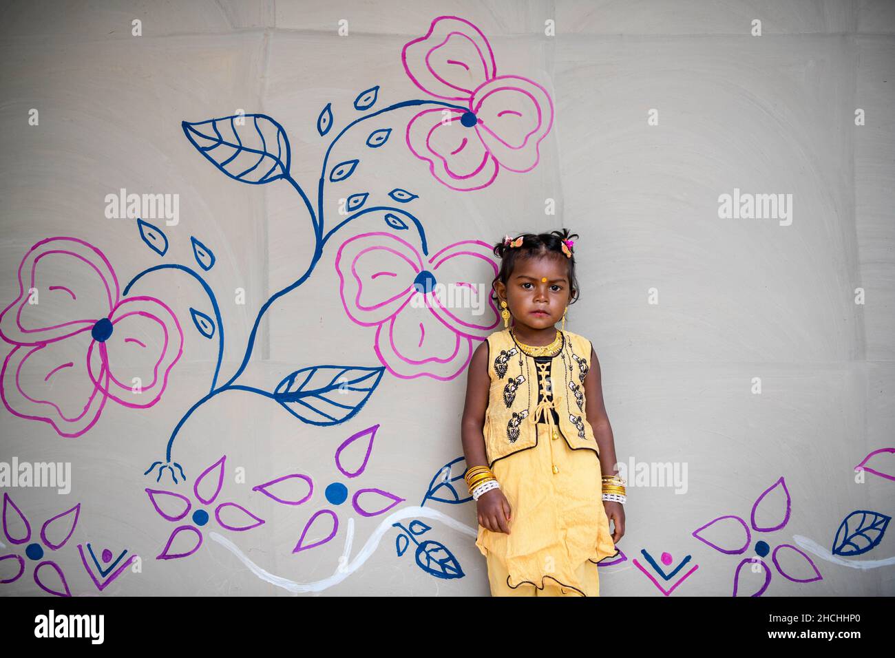 Rajshahi, Bangladesh. 25th Dec, 2021. A child poses for a photo in front of her painted house in Rajshahi. Santal tribe is an ethnic group native to eastern India. Santals are the largest tribe in the Jharkhand state of India in terms of population and are also found in the states of Assam, Tripura, Bihar, Odisha and West Bengal. They are the largest ethnic minority in northern Bangladesh's Rajshahi Division and Rangpur Division. Credit: SOPA Images Limited/Alamy Live News Stock Photo