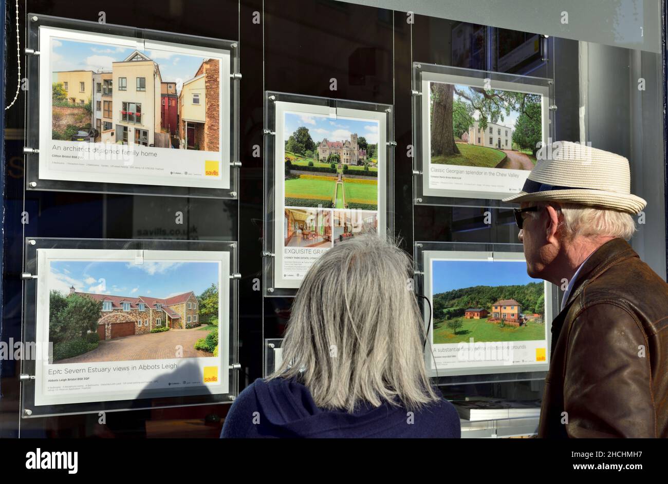 Older couple looking in estate office window at property descriptions, UK Stock Photo