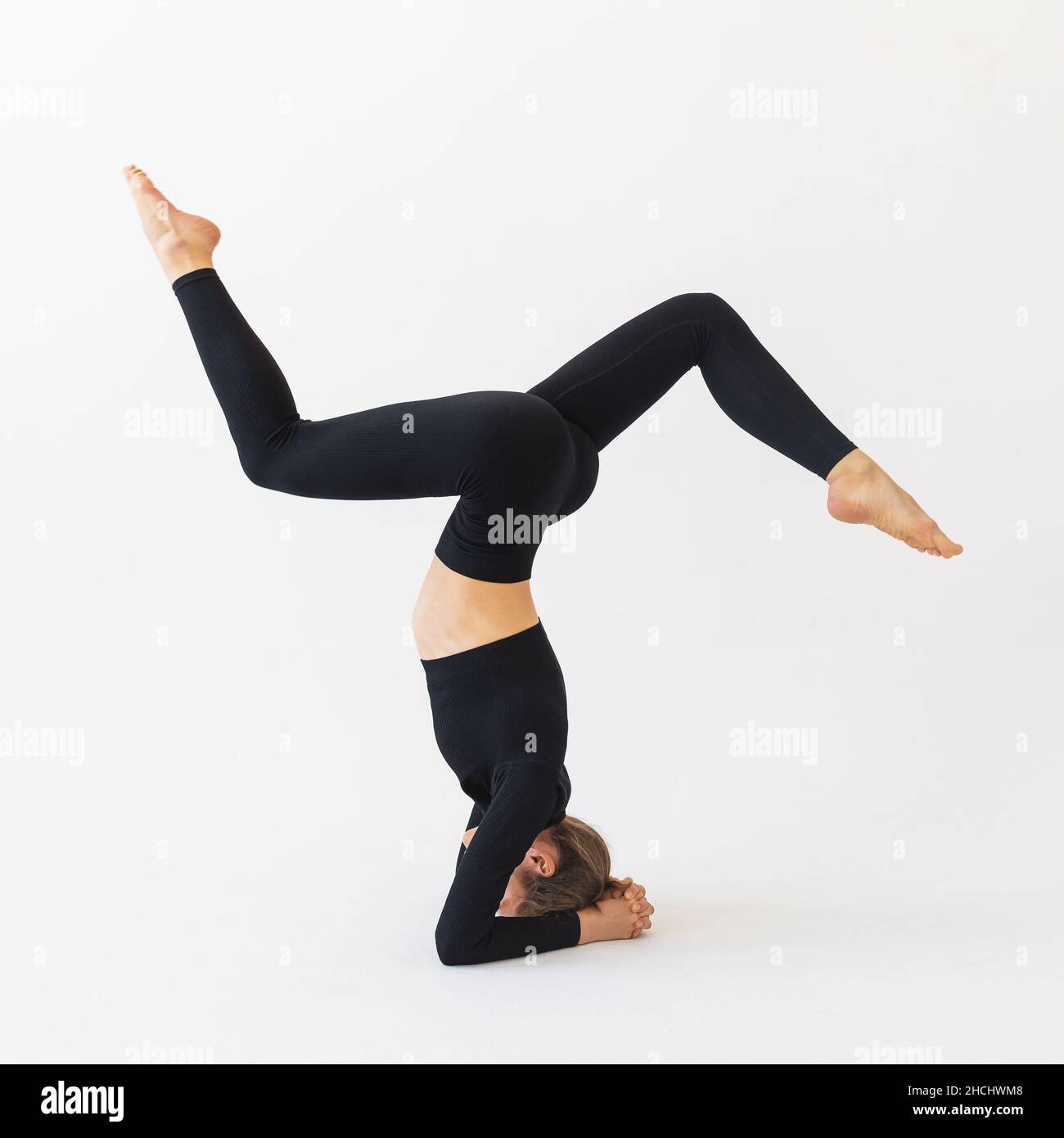 A young woman in black sportswear, performs a variation of the shirshasana exercise, trains in the studio on a light background Stock Photo