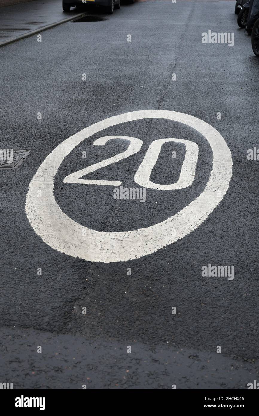 Twenty miles per hour (20 mph) road sign. 20 painted in white road paint, with a white circle around it, on a black gray paved street. Stock Photo