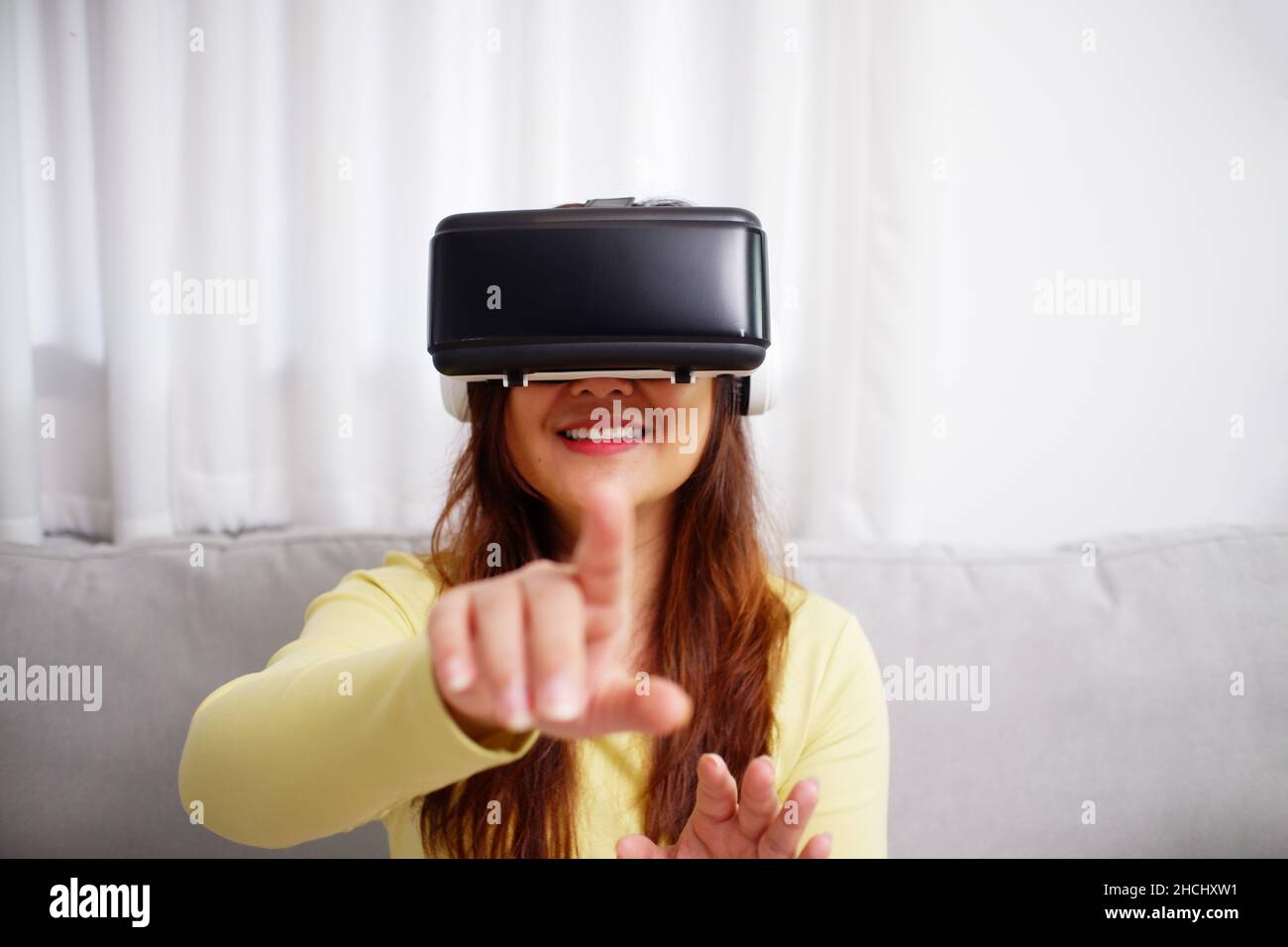 Young asian woman wearing virtual reality glasses, hand touching the air. VR headset. VR concept. Home entertainment. Stock Photo