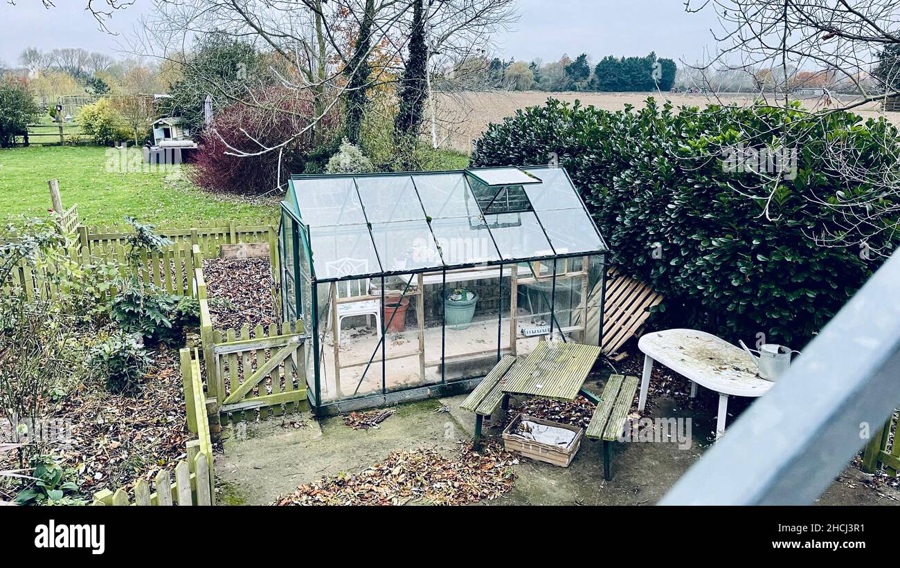 Tiny greenhouse surrounded by a yellow wooden fence with an alcove in