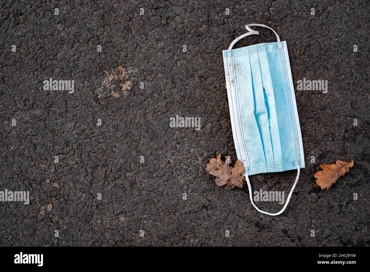 Medicine mask lying on the asphalt next to two autumn leaves Stock Photo