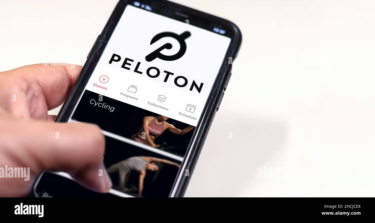 New York, USA, July 2021: A hand holding a phone with the Peloton app on the screen isolated on a white background. Peloton is an American exercise eq Stock Photo