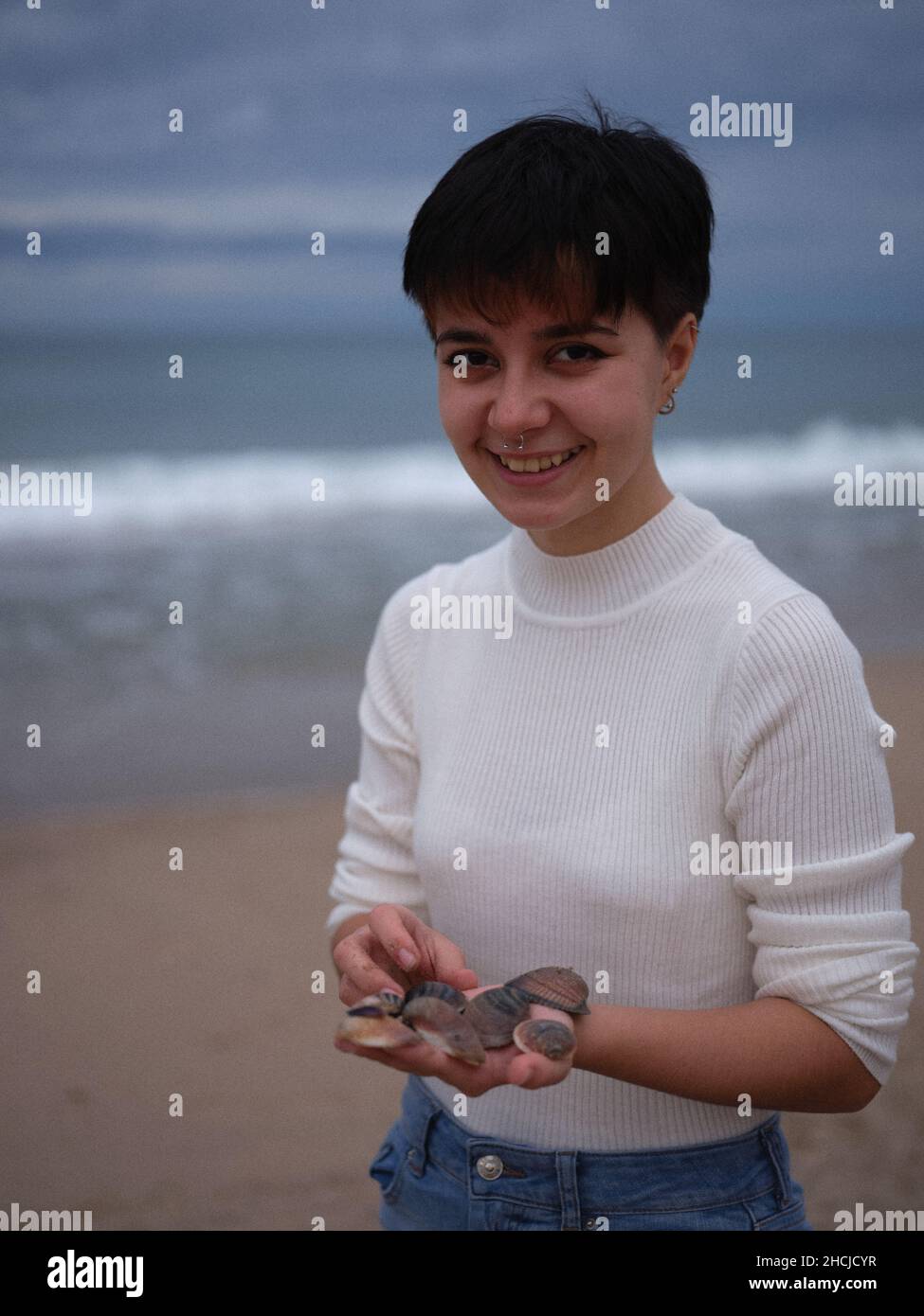 transgender looking at the camera with a white sweater and seashells in her hands Stock Photo
