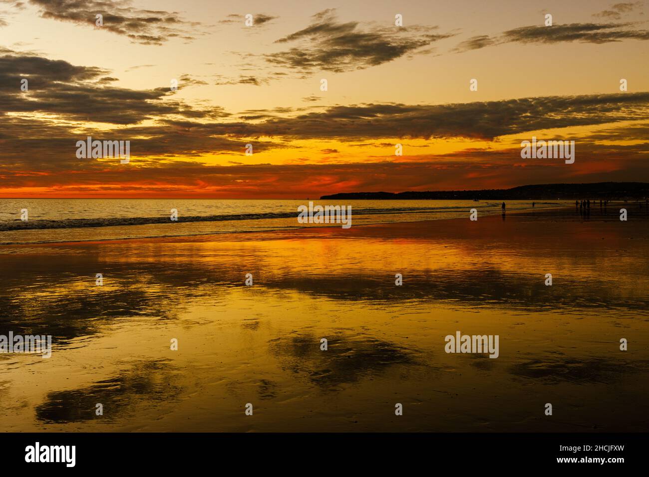 a dramatic sunset over the ocean with rays reflected on the water and small cloud pockets in the sky Stock Photo