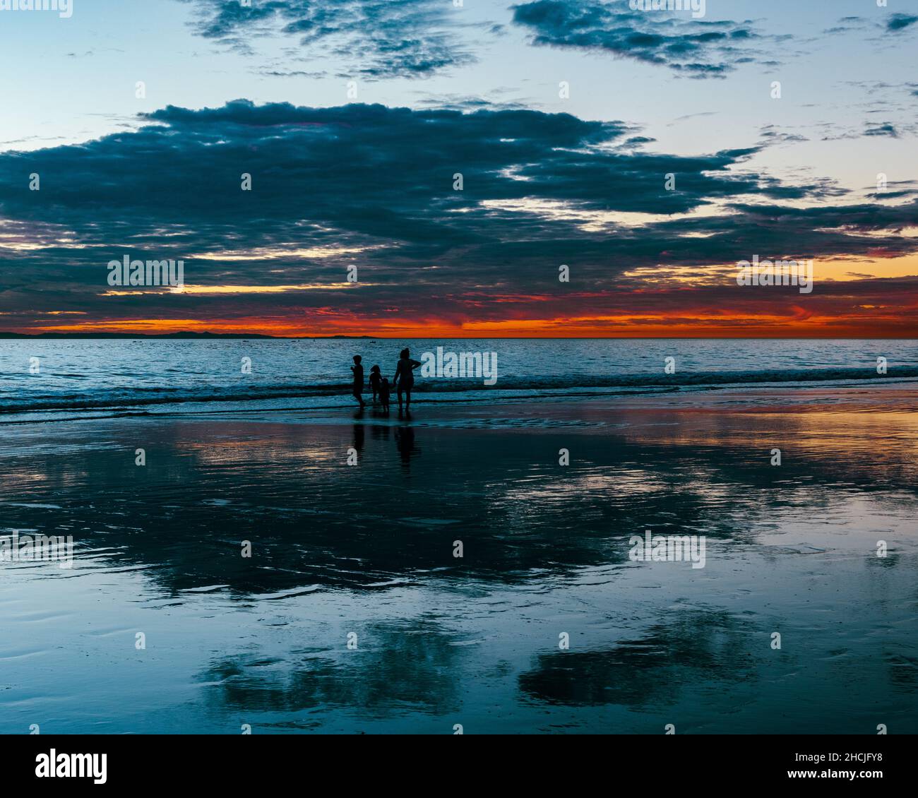 Silhouette of three people enjoying late sunset at west coast beach, California Stock Photo