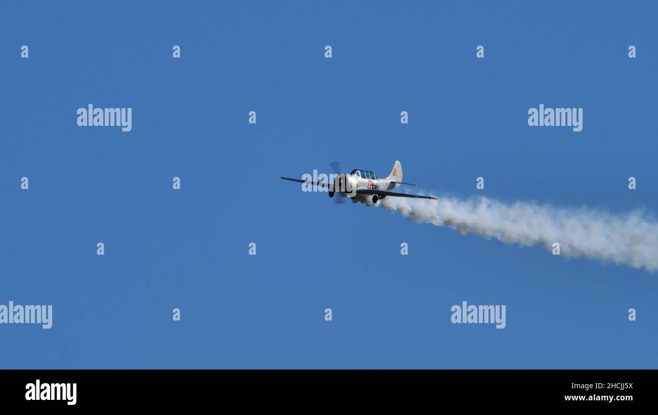 Thiene Italy OCTOBER, 16, 2021 Single metallic propeller airplane made in Russia during the soviet era in the blue sky with white smoke. Copy Space. Yakovlev Yak-52 by YAK Italia Stock Photo