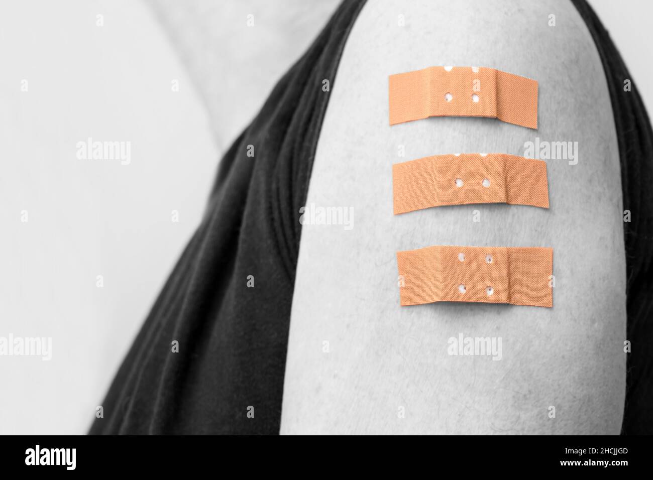 Human arm with three medical plasters after vaccinations against covid-19, initial immunization, repeat and third booster dose, color key - black and Stock Photo